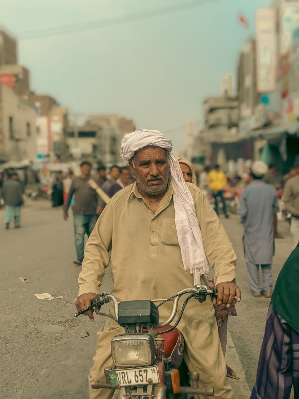 photo of a man wearing a turban on motorbike in a busy downtown street